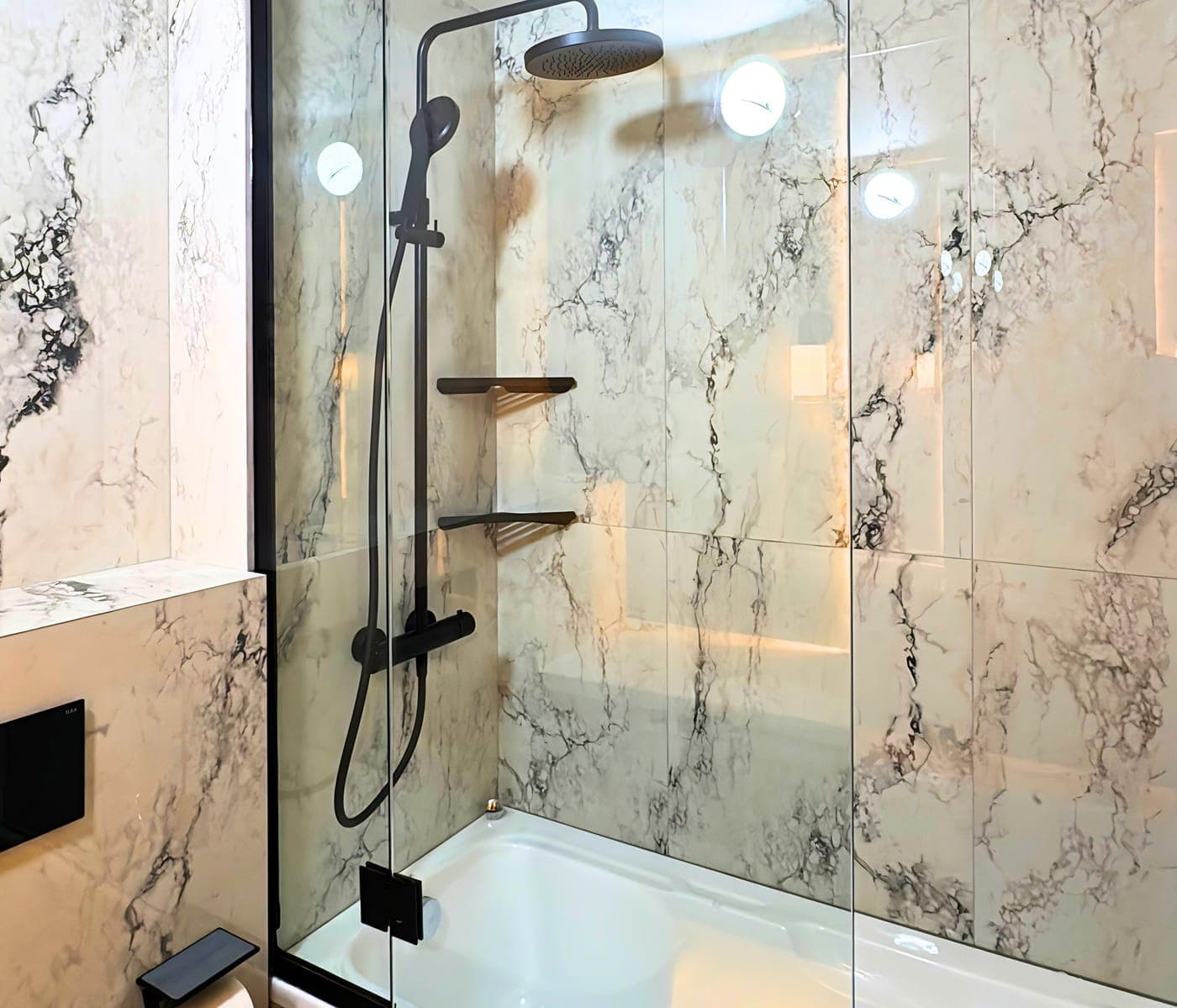 Clear glass bath screen with black fittings over a white bathtub in a marble bathroom