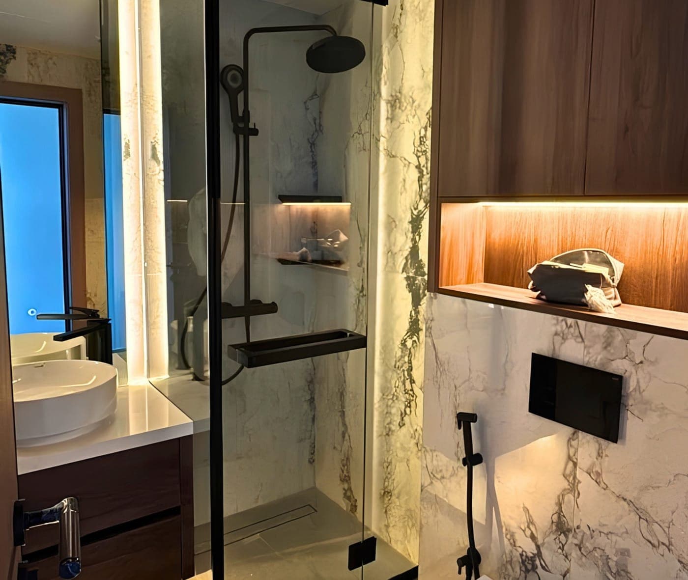 Glass shower enclosure with black frame and fittings in a marble-clad bathroom