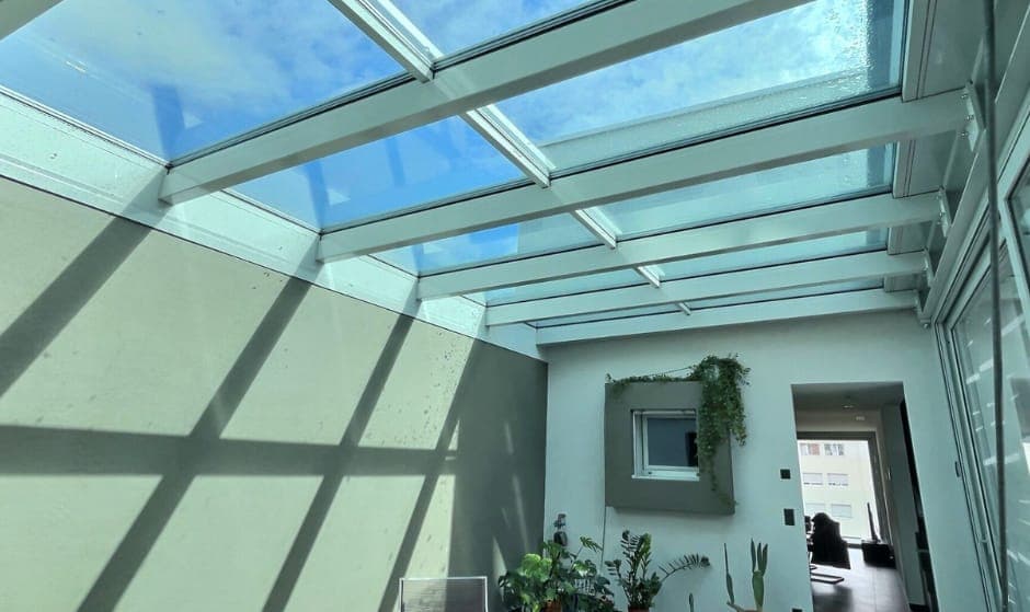 Aluminium-framed glass roof over a courtyard, casting grid shadows on the walls
