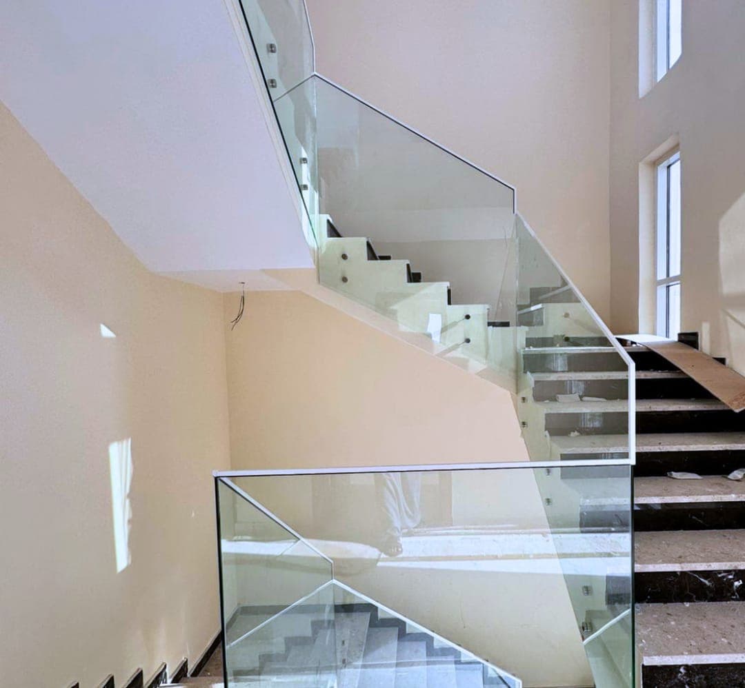 Frameless glass balustrade fixed along a marble staircase in a double-height hall